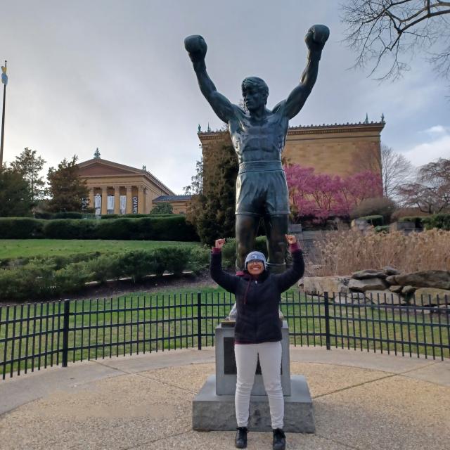 Merlin standing in front of Rocky Statue with fists in the area in front of the steps where the Rocky movie scene was shot