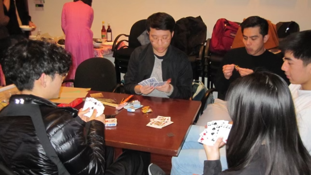 A group of five people playing cards at a table.