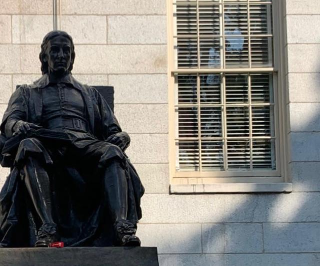 This is a picture of the top of teh John Harvard Statue, which shows only the shape of the statue itself, and not the base with it's description. The statue shows a man posing in a sitting, very academic looking, position. 