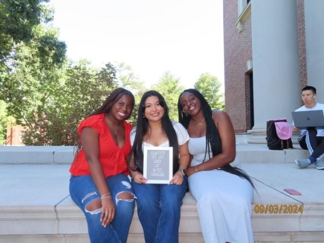 My friends and I sitting on the steps of Widener Library, holding a sign that says "Happy First day of 14th Grade"."