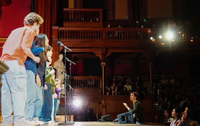 Performers on stage with microphones, while an audience watches.