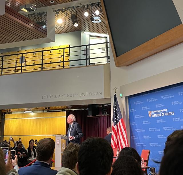 A picture of the main lobby of the Kennedy School building. It is decorated and full of students listening to Bernie Sanders speak.