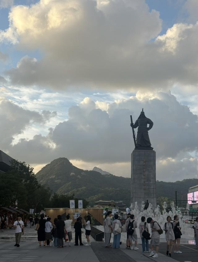 Picture of a plaza in the afternoon with a statue and people walking around