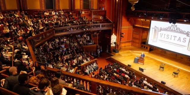 A lecture held in Sanders Theater with the word VISITAS projected onto a screen.