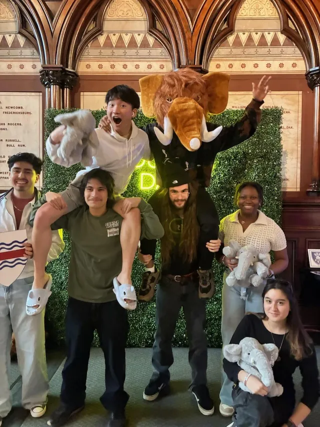 A group of first-years taking pictures in front of a housing day backdrop in Memorial Hall