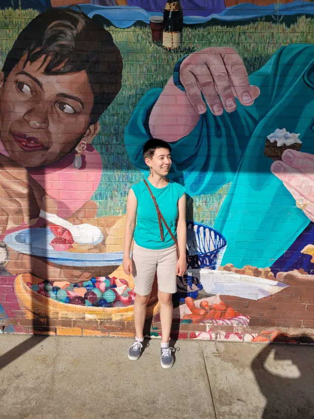 A student stands in front of a colorful mural
