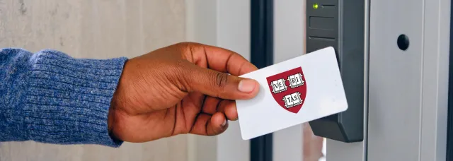 A hand holding a card featuring a Harvard ID with the Harvard crest