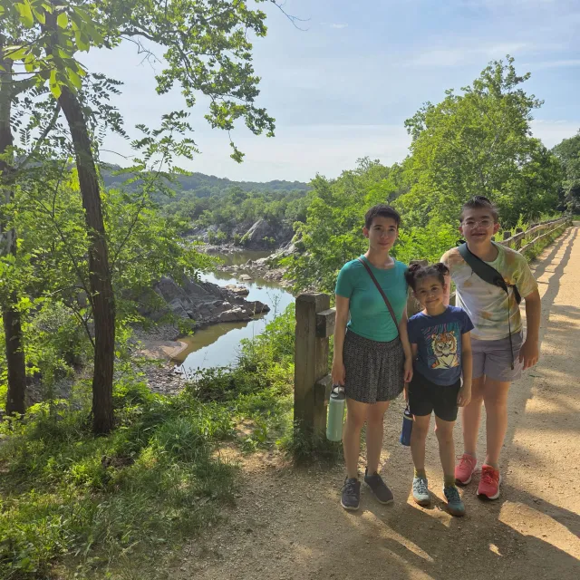 Three siblings stand in front of an overlook that looks down on a river.