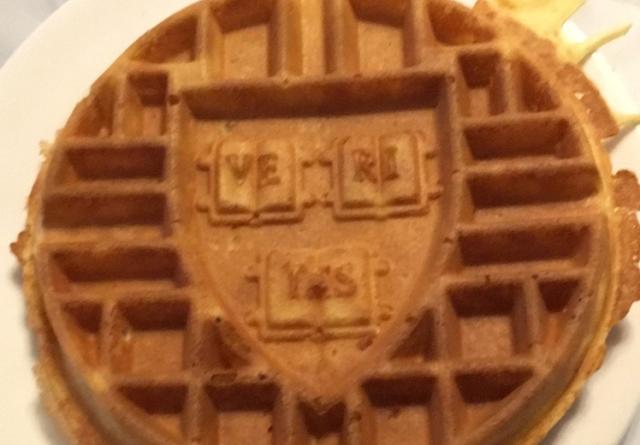 A waffle sits on a plate with the Harvard "veritas" crest imprinted in the center.