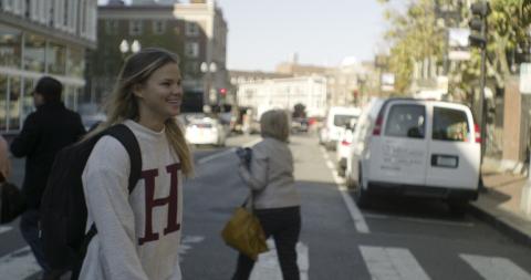 Student wearing Harvard sweatshirt walking towards Harvard Yard