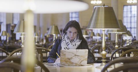 Female student working at a laptop in Widener library 