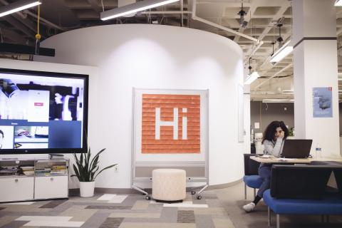  A student sits at a laptop in a computer lab. A whiteboard is covered with post-it notes placed in the shape of the Harvard Innovation Lab logo.