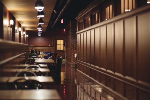 Two students sit in an otherwise empty dining room, lined with dark wood panels.