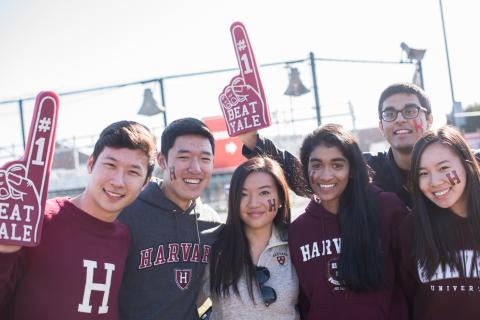 Six Harvard students with foam fingers cheering for Harvard-Yale football game