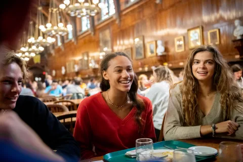 Three students smiling and eating in Annenberg Dining Hall