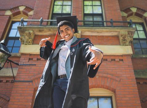 student posing with cap and gown on in front of a building
