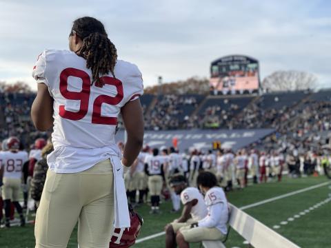 A student athlete watches his teammates on the sidelines during the final moments of the 2021 Harvard-Yale game.