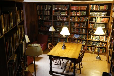 Private library room with a table, lamps, and walls of book shelves