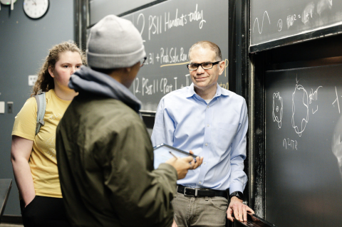 Professor consults with two students standing at the blackboard.
