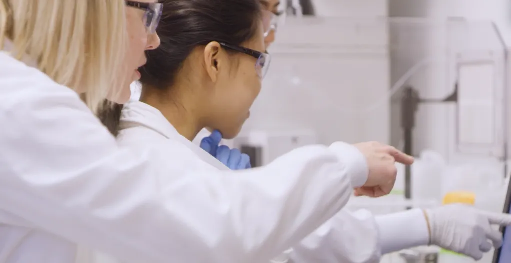 A professor and two students in white lab coats doing research in a lab
