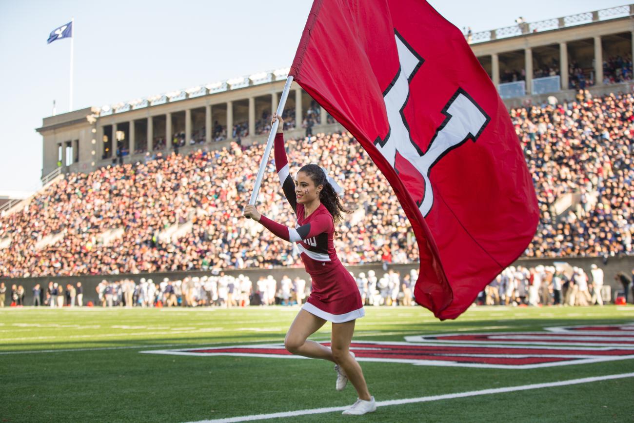 A Harvard cheerleader waving a Crimson flag in Harvard Stadium filled with fans