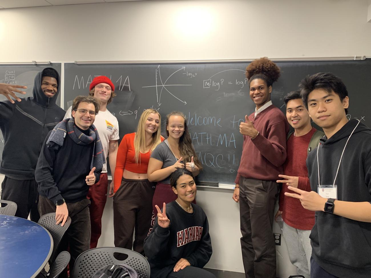 Students and course assistants gathered around a chalkboard, posing for a picture
