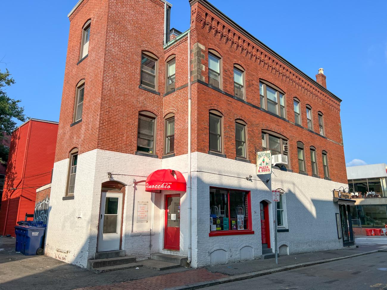 Photo of Pinocchio's Pizza & Subs located in a brick building with the bottom half painted white and red and the top half left unpainted.