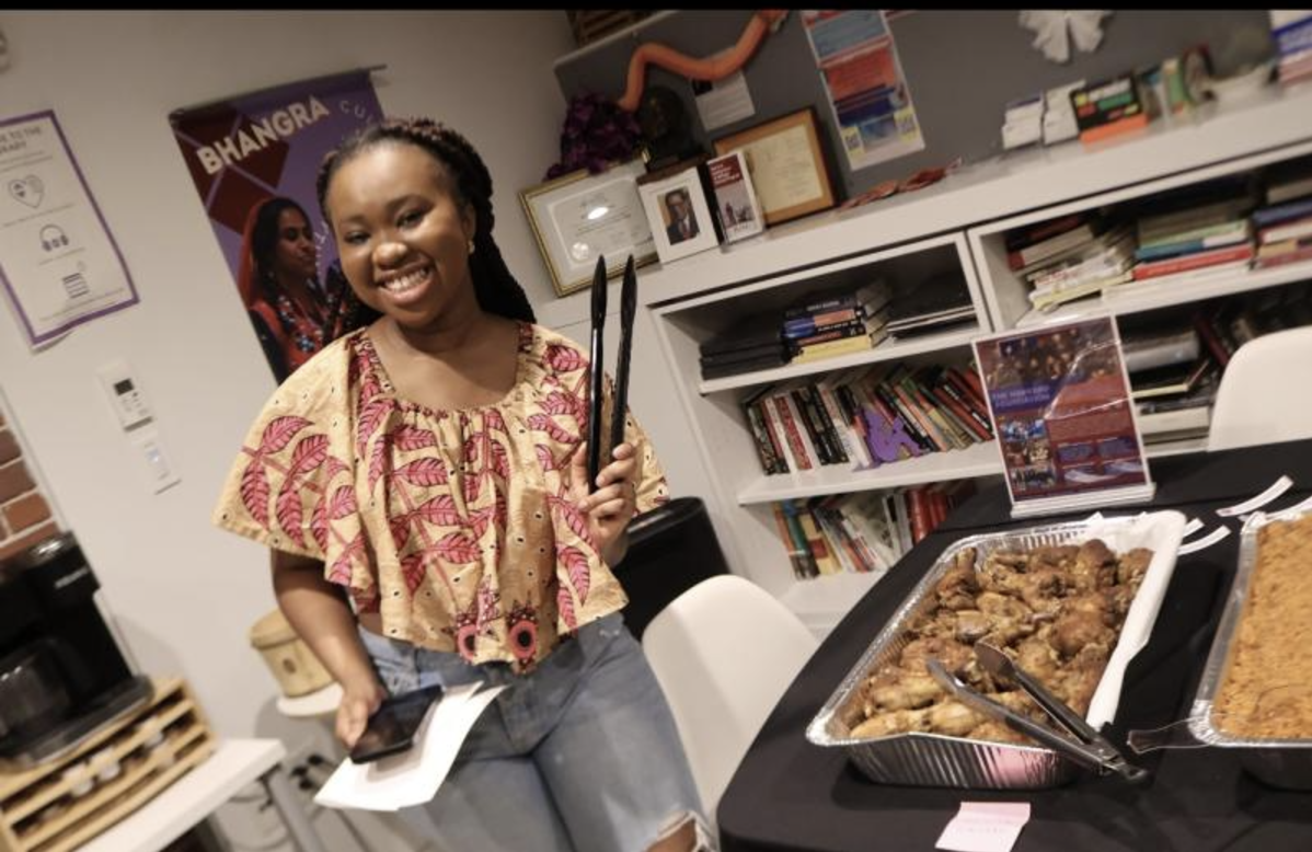 A girl smiling at the camera while holding kitchen tongs. There is a plate of chicken next to her.