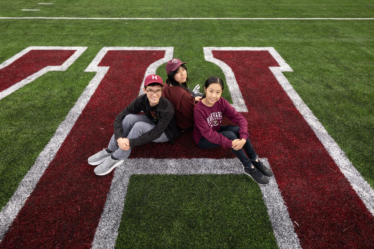 Three students sitting on the Harvard H on a football field.