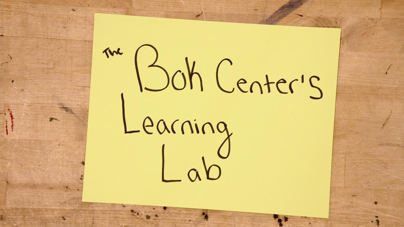 A yellow sticky note that reads "The Bok Center's Learning Lab" placed on a wooden surface.