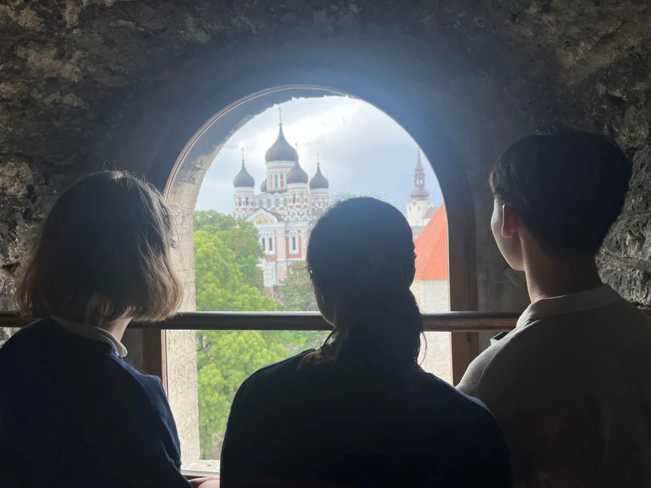 Three students looking out an open window at the top of one of the belltowers.