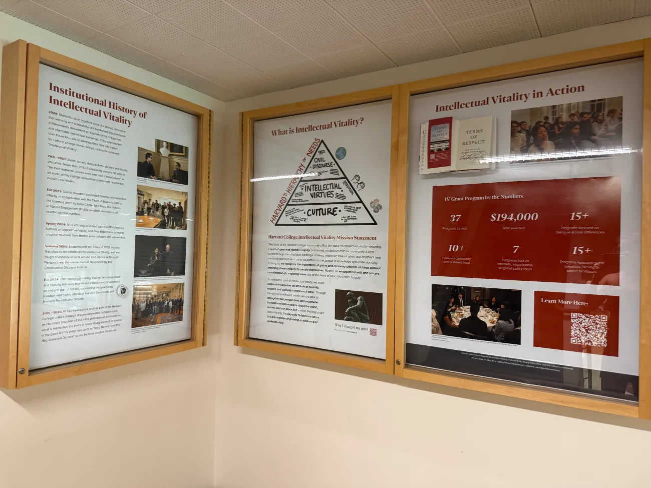 Three wooden framed display cases on a wall featuring posters and photos detailing Harvard's Intellectual Vitality initiative.