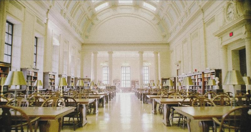 Interior shot of a Harvard Library, a large white room with a single studying student.