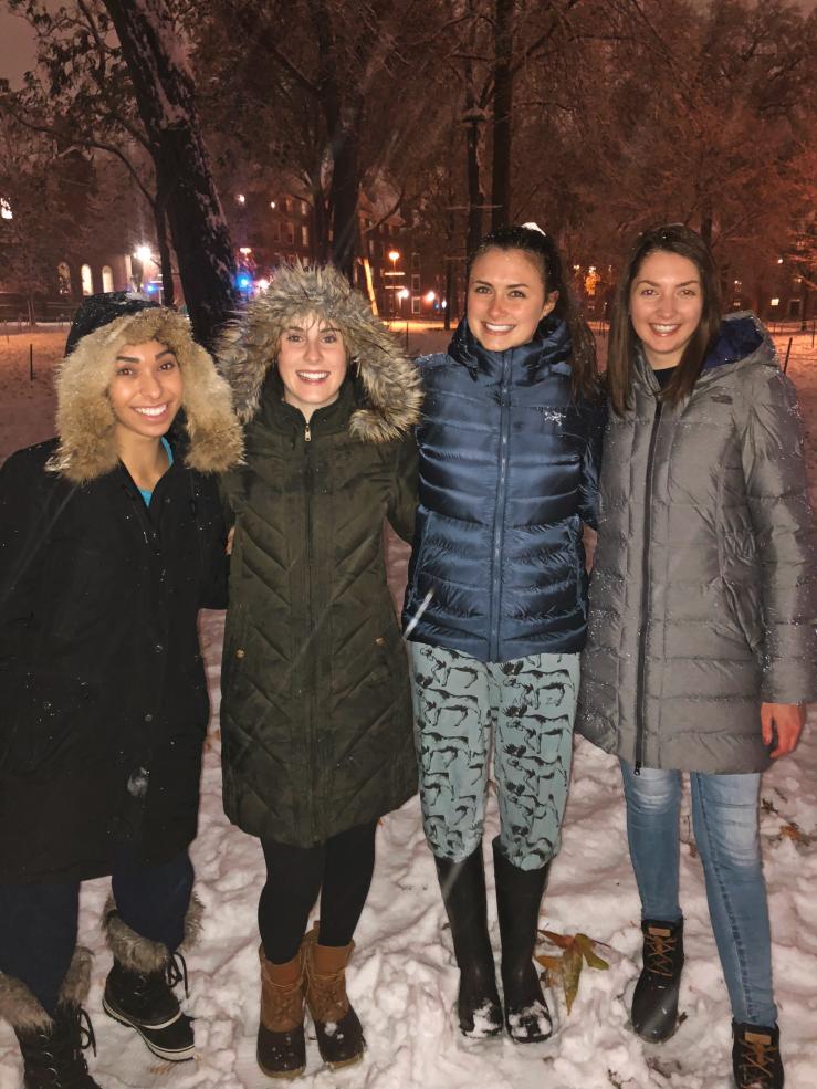 Four girls outside in winter coats, snow falling