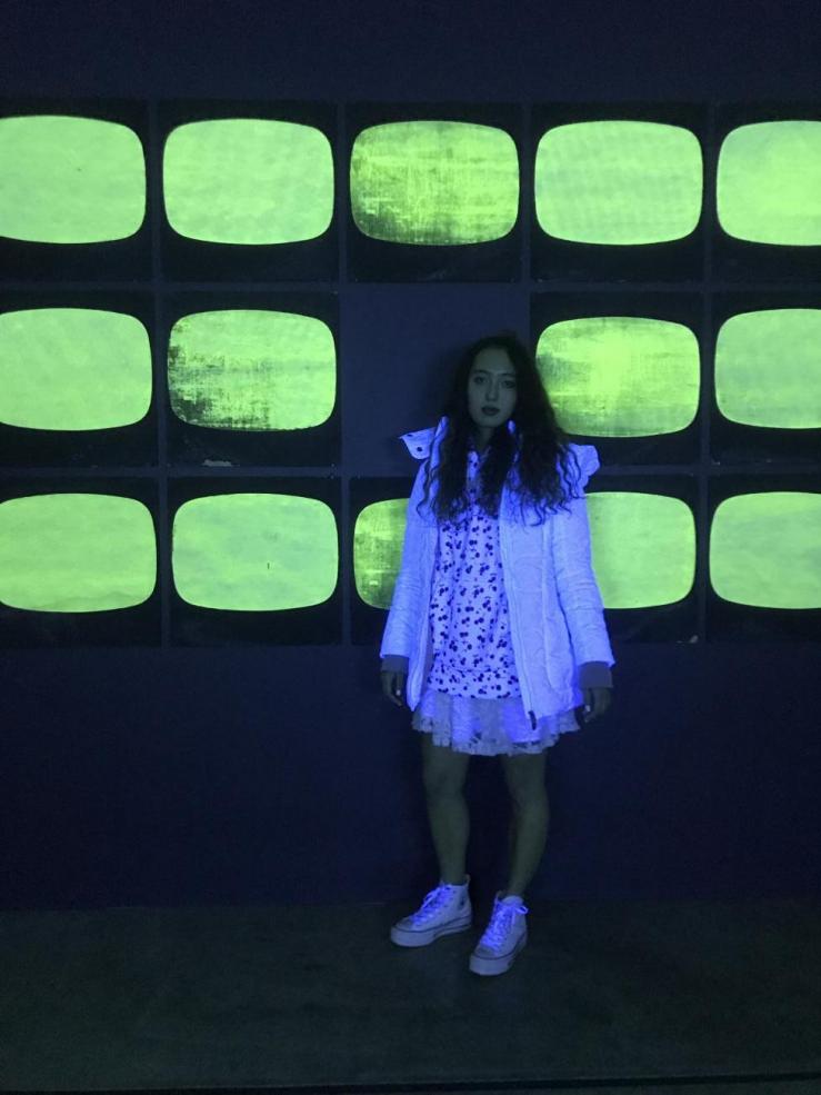 Alian standing in front of her art project - a neon green wall lit up by blacklights