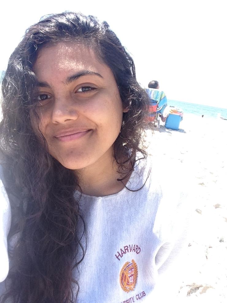 Me on a beach wearing a gray Harvard sweatshirt that says "Harvard Varsity Club" on it.