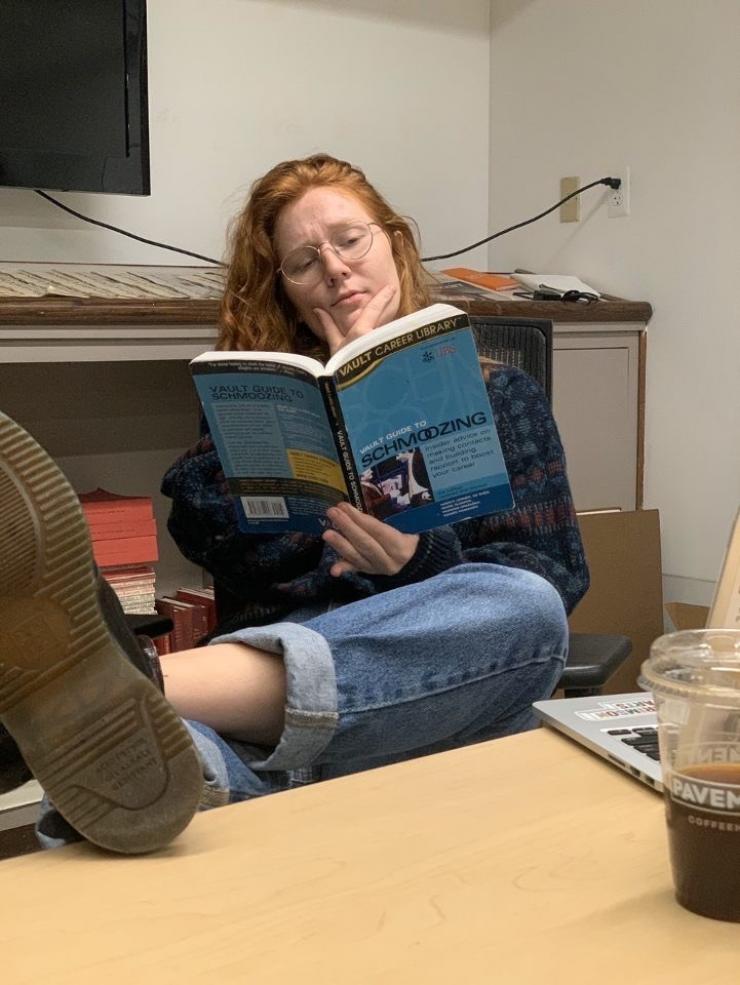 me holding a book titled "schmoozing" with my feet up on a table in the building of The Harvard Crimson