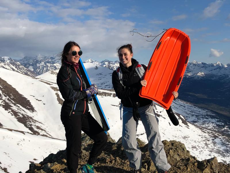 Two girls holding sleds on a mountaintop