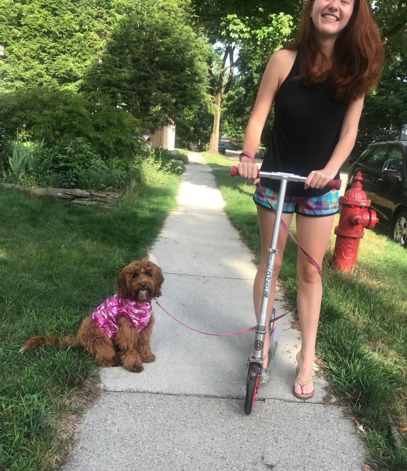 Girl riding scooter with dog next to her