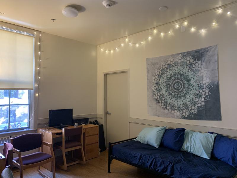 A dorm common room with a futon, desk and lights. 