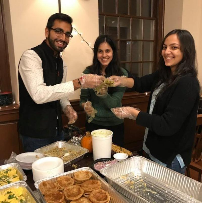 Three college students indoors holding up Indian food