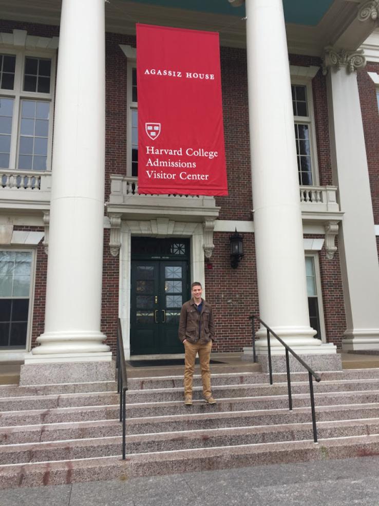 A student posing in front of the Harvard Visitors&#039; Center