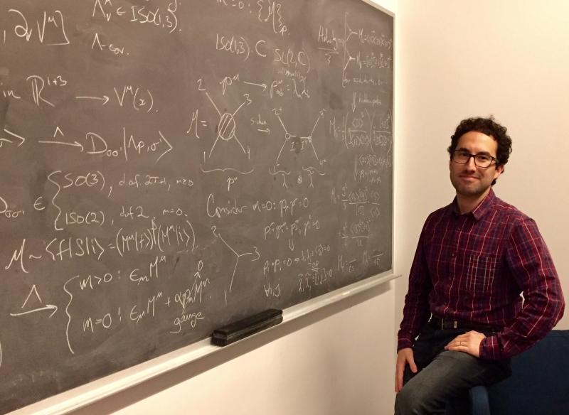 Preceptor Camille Gomez-Laberge stands in front of a chalkboard in his office.