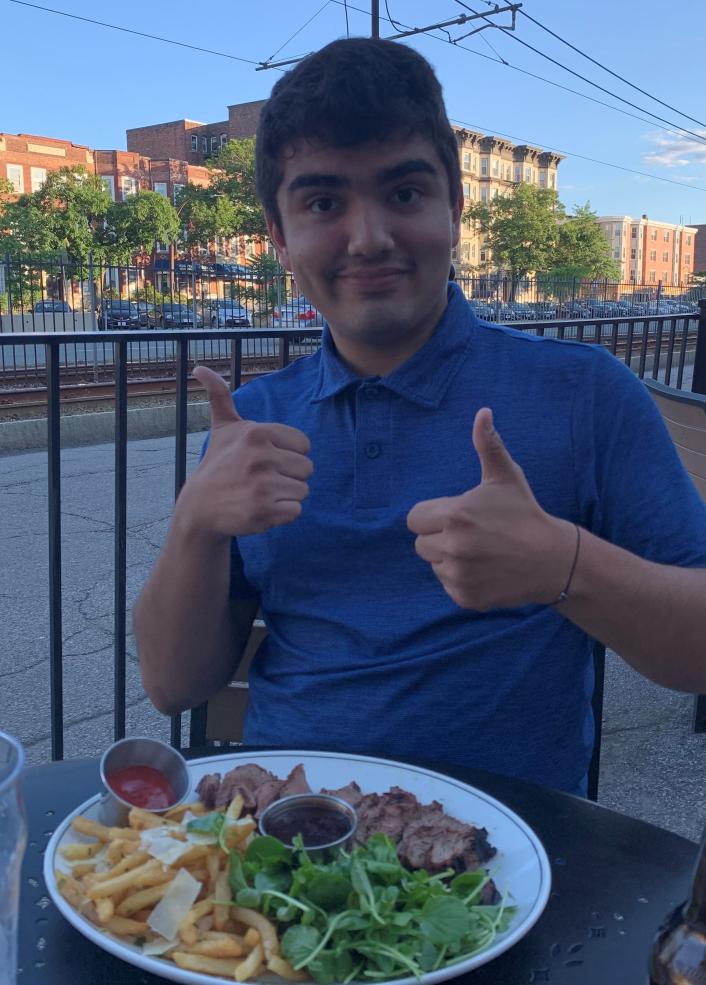 A man showing thumbs up and eating food outside.