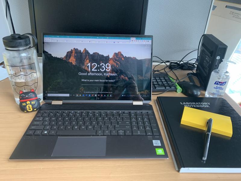 A laptop computer, lab notebook, and sticky notes on a desk.
