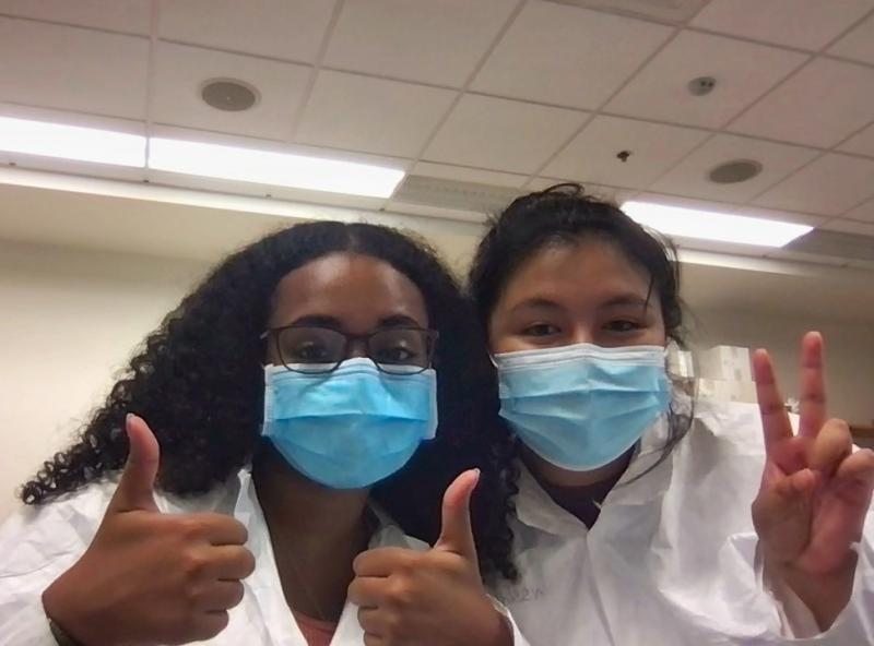 Two girls holding up peace signgs wearing lab coats.