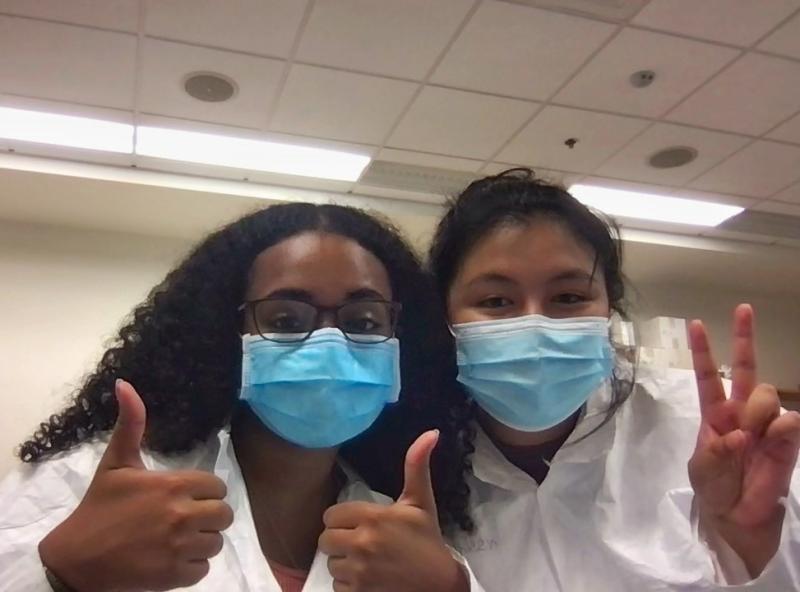 Two girls holding up peace signgs wearing lab coats.