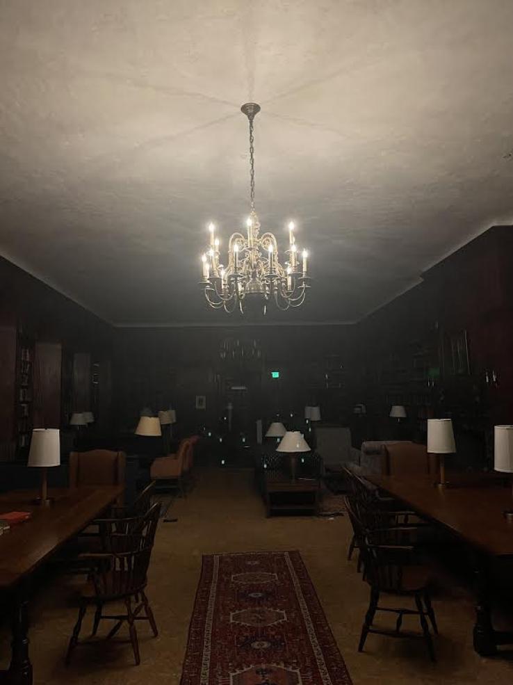 A photo of Lowell Library. All the lights are off except for a chandelier in the center of the room.