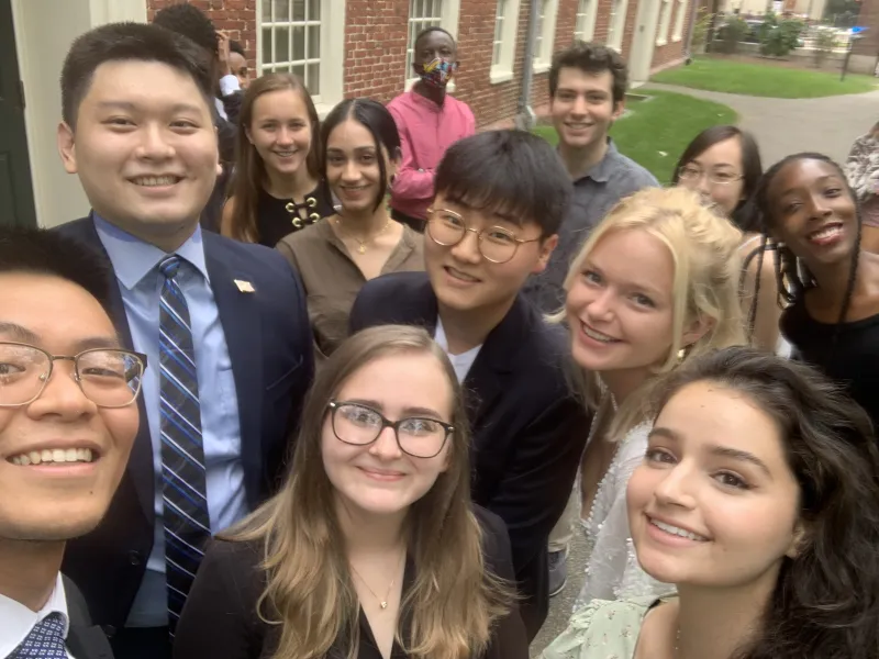 Selfie picture of Mass Hall residents standing in front of Mass Hall, smiling at the camera,.