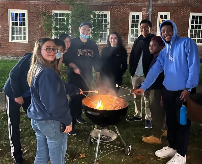 Picture of Mass Hall residents roasting marshmallows at a fire pit and smiling at the camera.